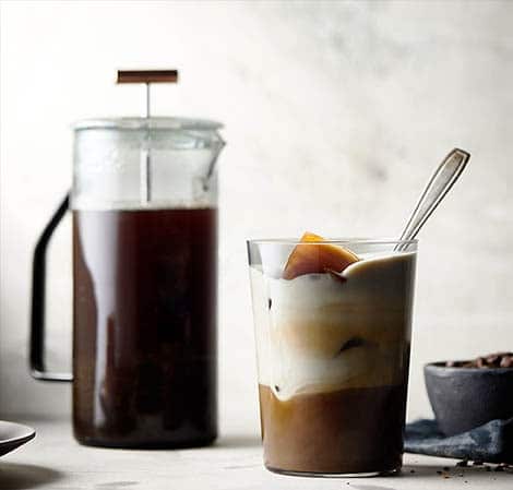 Cold-brew cappuccinoa lasissa, taustalla kannussa cold-brew kahvia